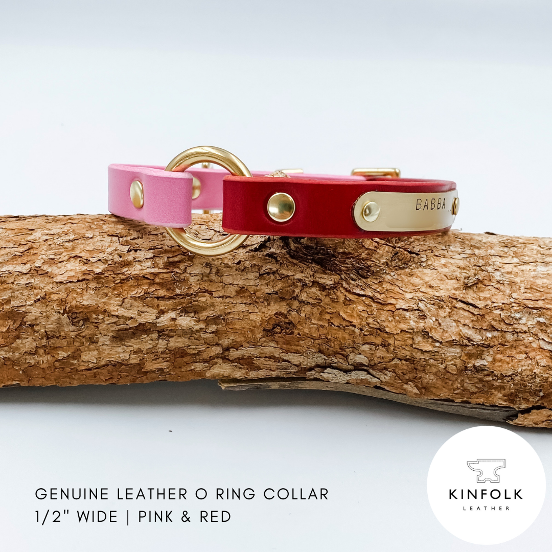 Pink and red leather collar with gold hardware on a wooden log, branded 'KINFOLK LEATHER'.