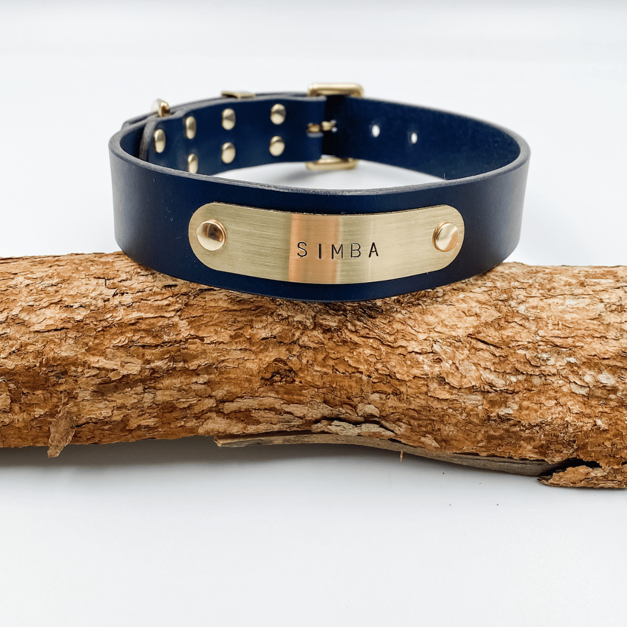 Navy blue leather dog collar with gold nameplate on a wooden log