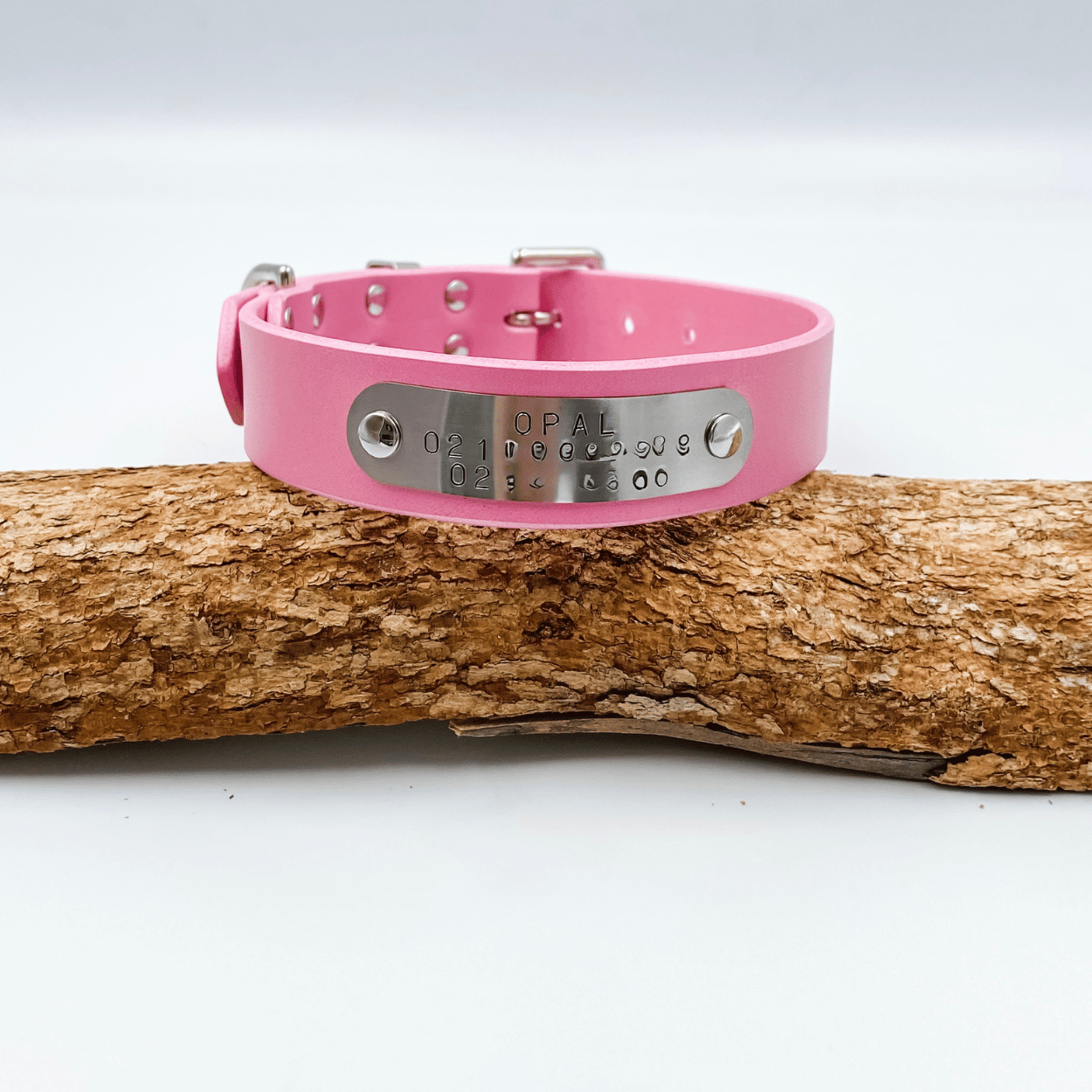 Pink dog collar with metal tag on a wooden log